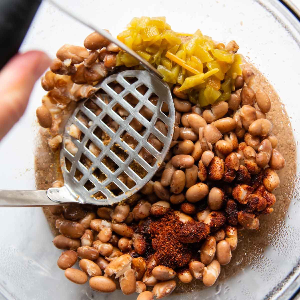 a potato masher mashing beans with seasonings.