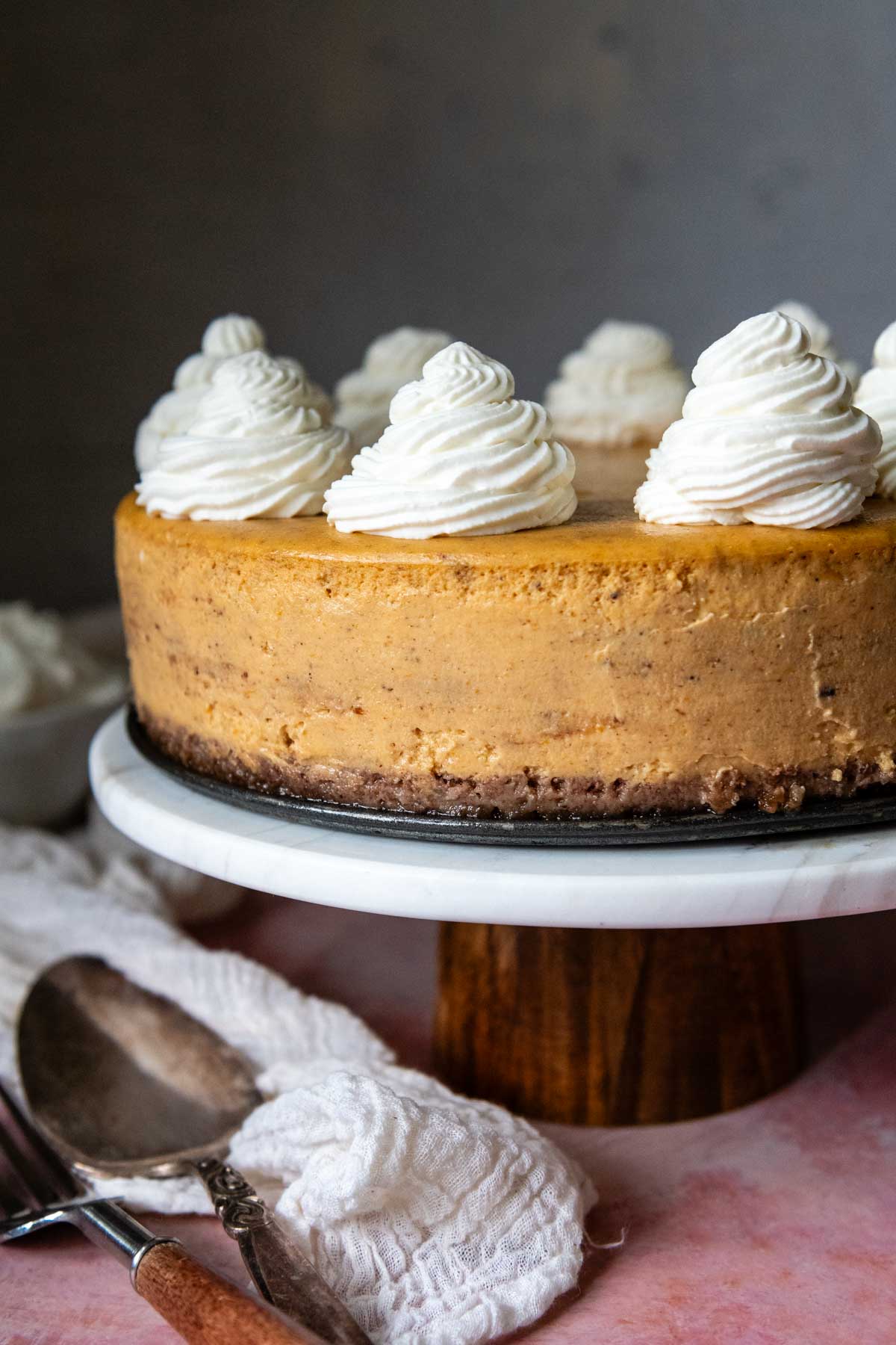 a pumpkin cheesecake on a cake stand with whipped cream piped on top.
