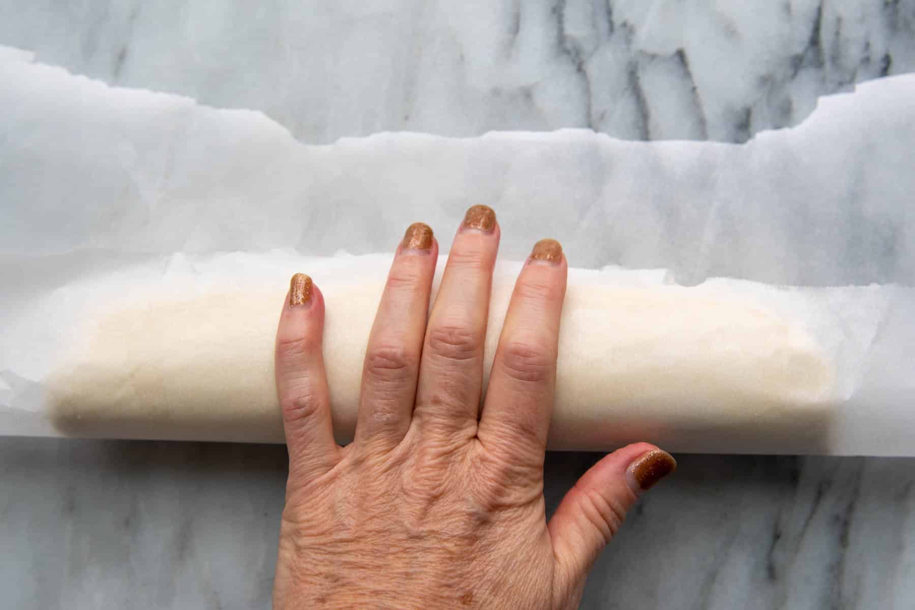 a hand rolling dough with parchment.