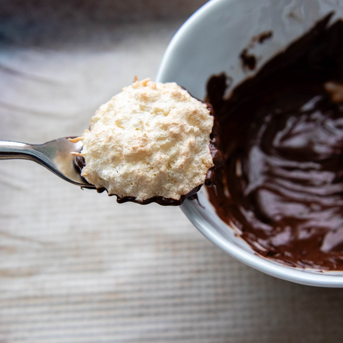 a macaroon coming out of a bowl of chocolate.