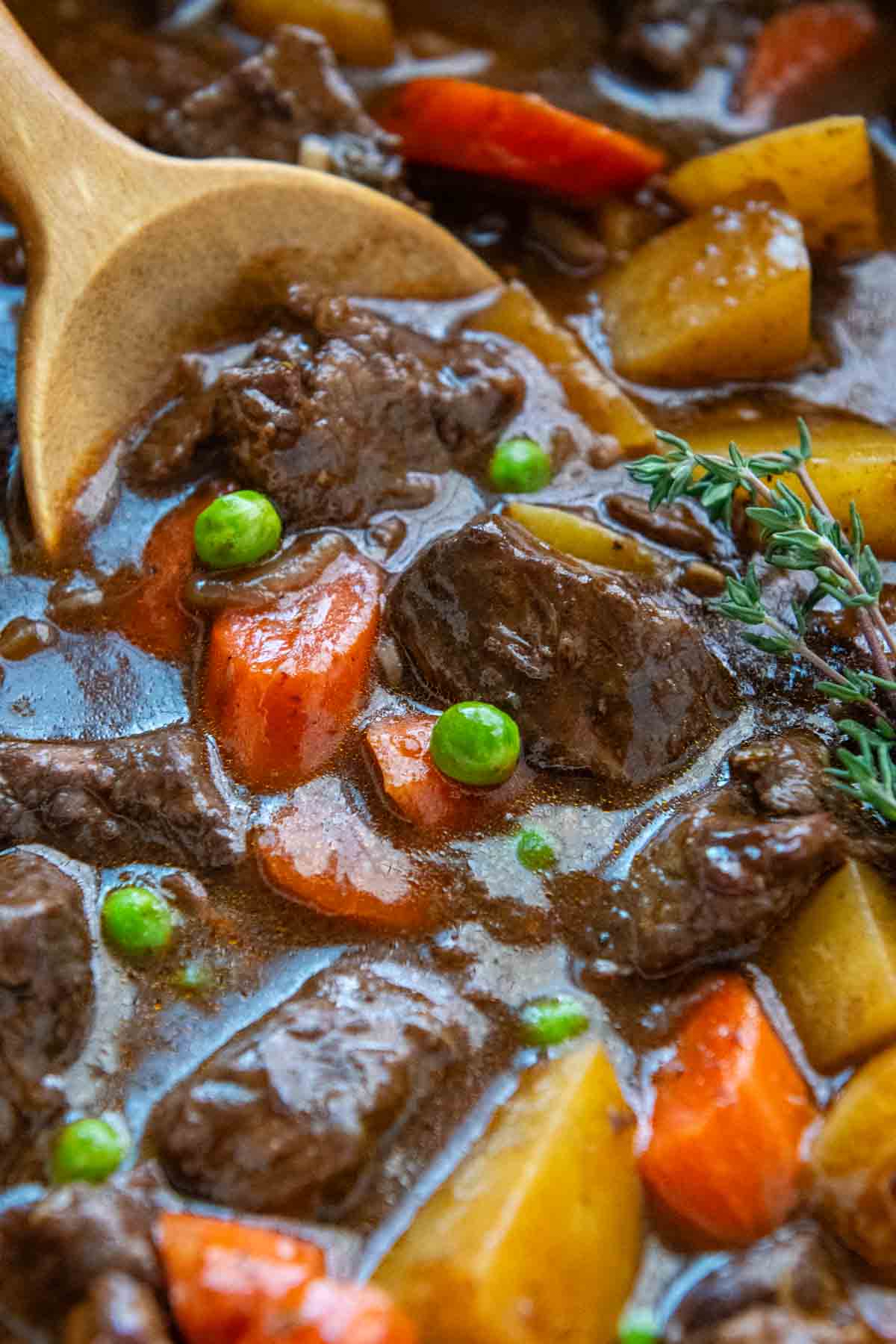 close up of a pot of beef stew with a wooden spoon.