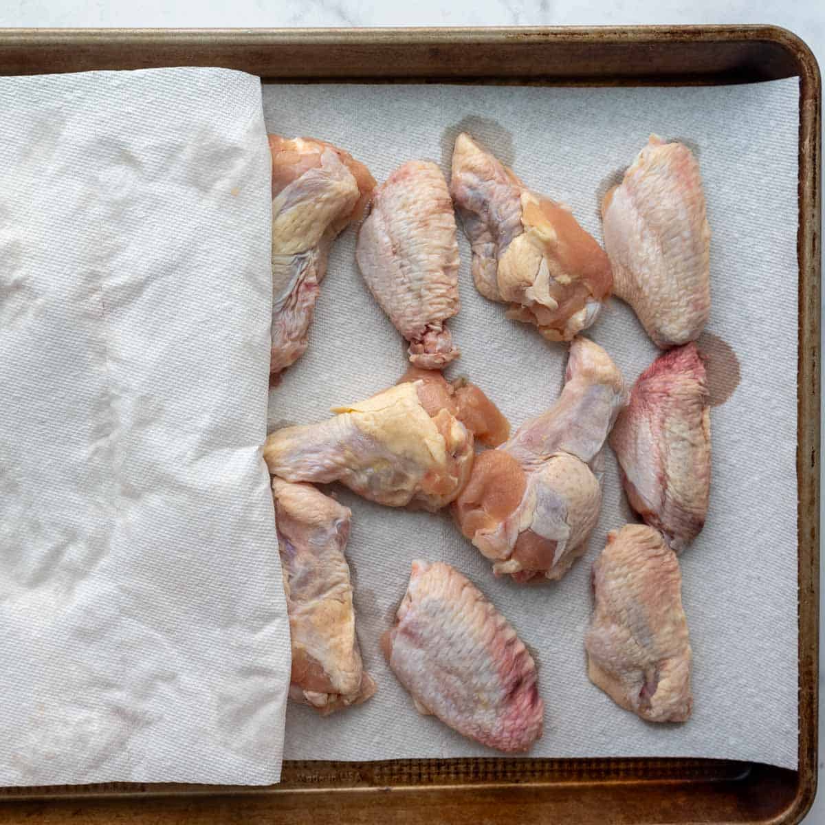 the wings being dried with paper towels on a baking sheet.