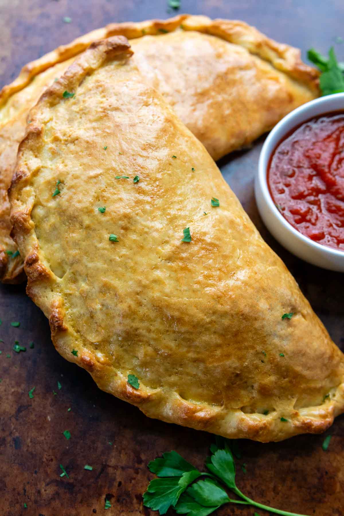 a baked calzone with a dish of pizza sauce next to it.
