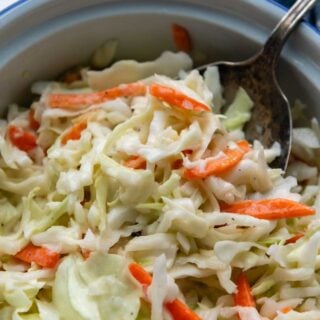 a spoon going into a bowl of coleslaw on a white marble surface.