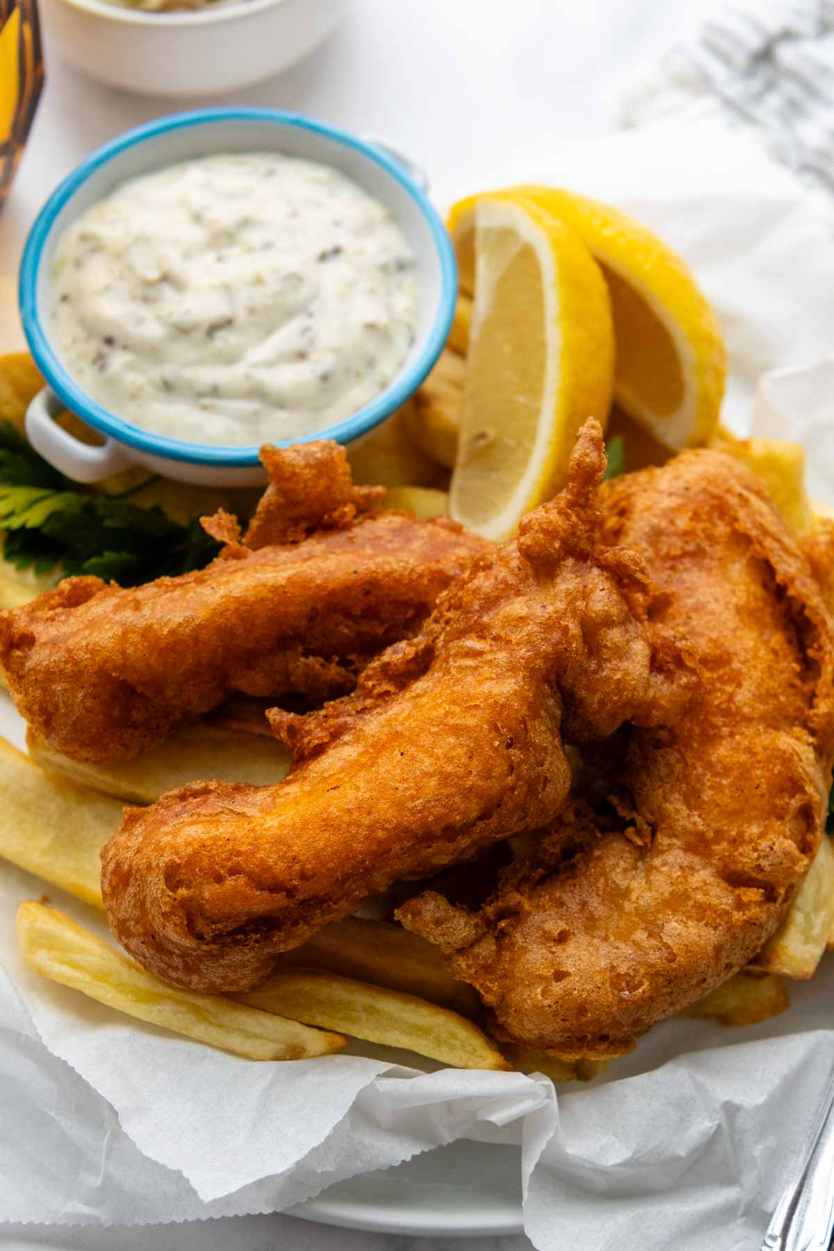 a serving of fish and chips with tartar sauce and lemons.
