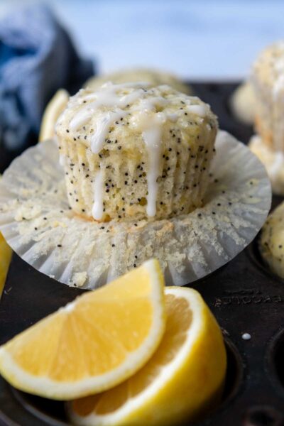 a lemon muffin with poppy seeds on an opened paper liner with glaze on top.