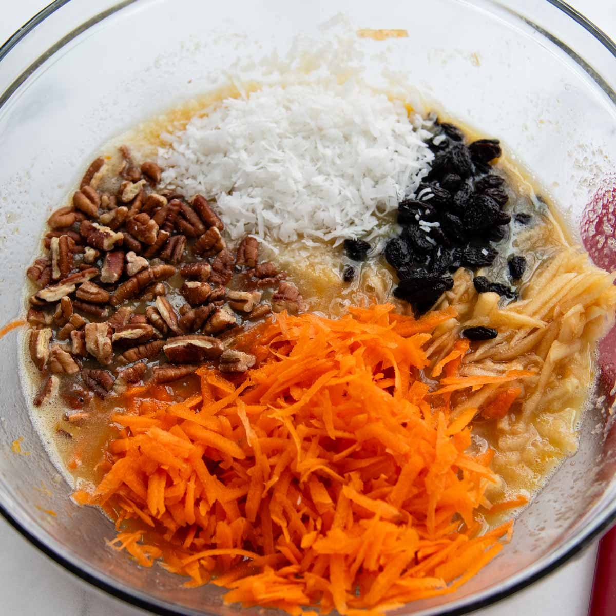 the wet ingredients in a bowl with grated carrots, apples, and other mix ins.