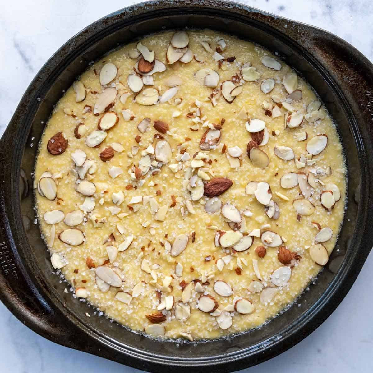 unbaked cake with sliced almonds and sugar on top.