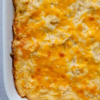 Cheesy gluten free hash brown casserole in a white baking dish.