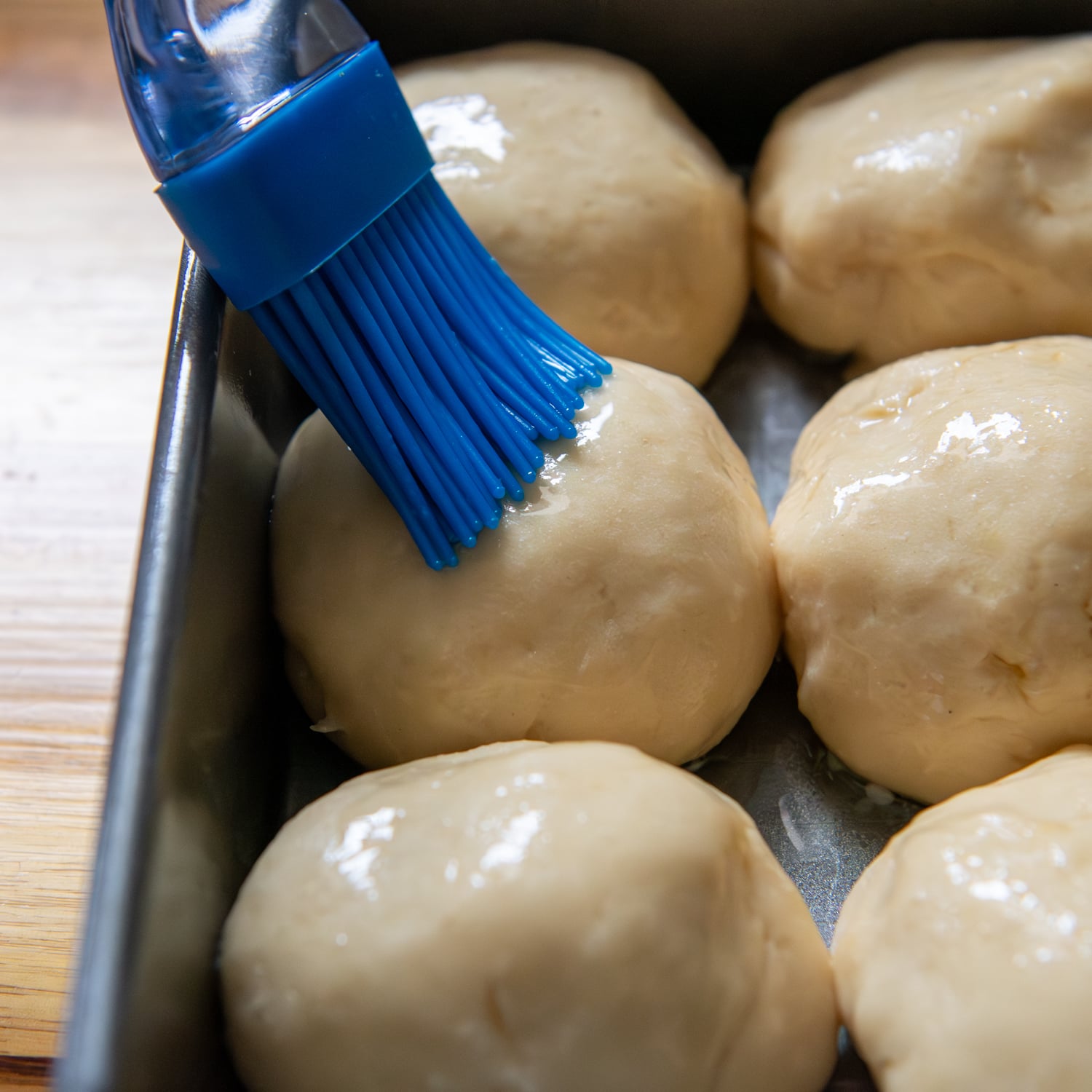 Blue brush painting melted butter on the tops of dough balls.