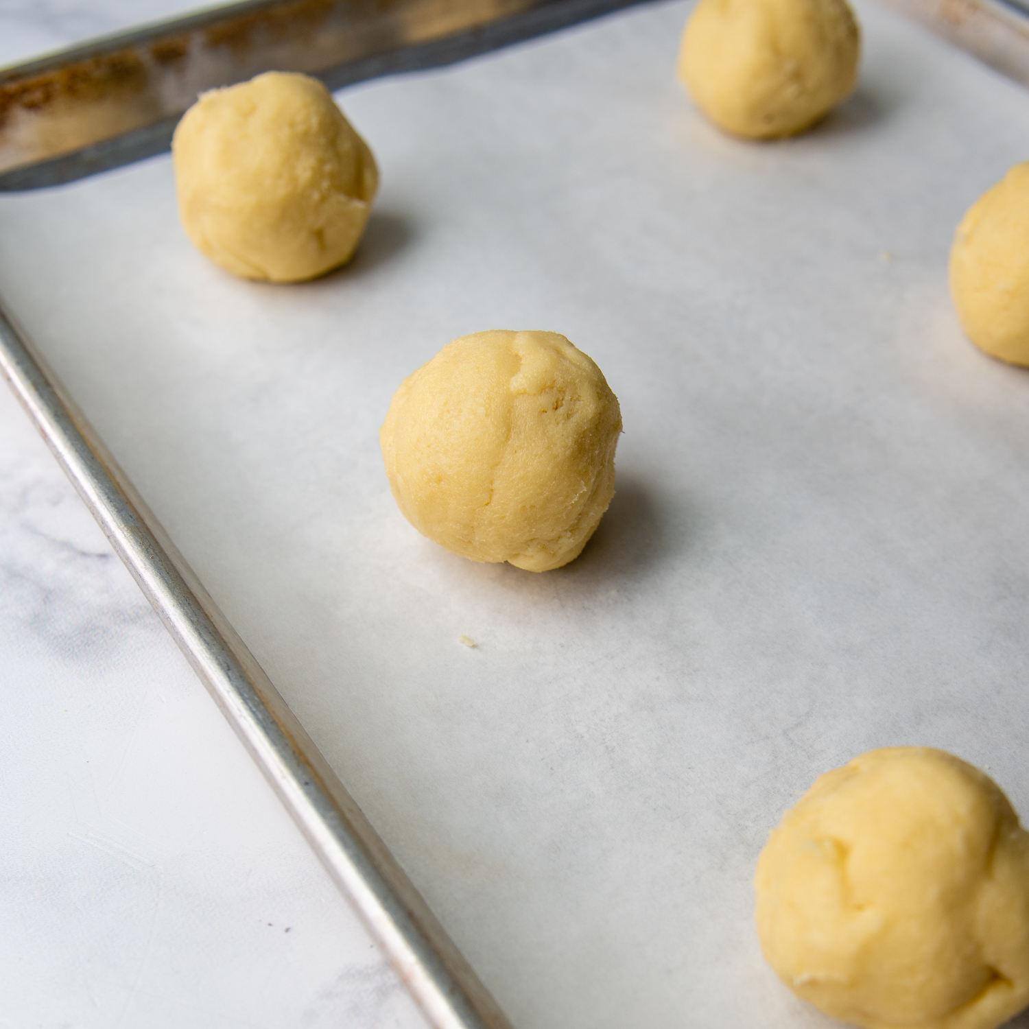 Formed cookie dough balls on parchment paper on a baking sheet.