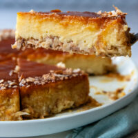A piece of coconut flan being lifted off of a white plate by a fork.