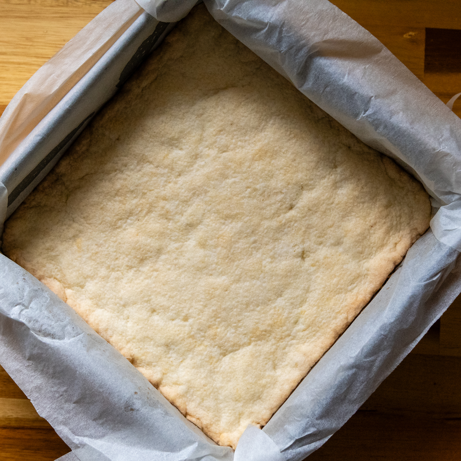 Baked shortbread layer in a pan with parchment paper.