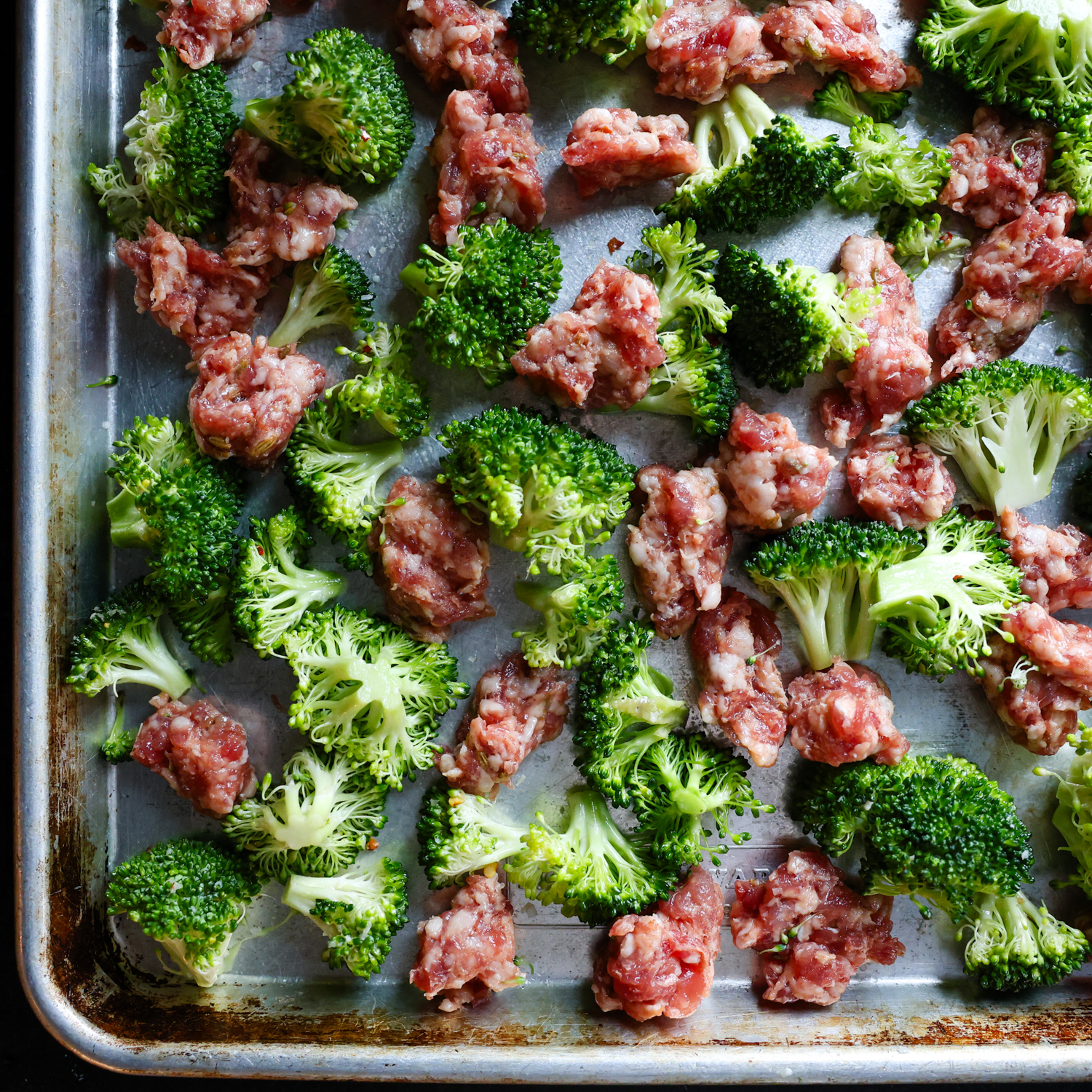 Raw broccoli and Italian sausage on a sheet pan.