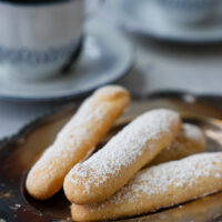 A pile of lady fingers dusted with sugar laying on a plate.