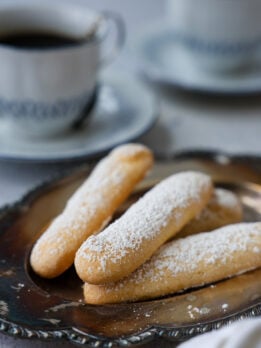 A pile of lady fingers dusted with sugar laying on a plate.