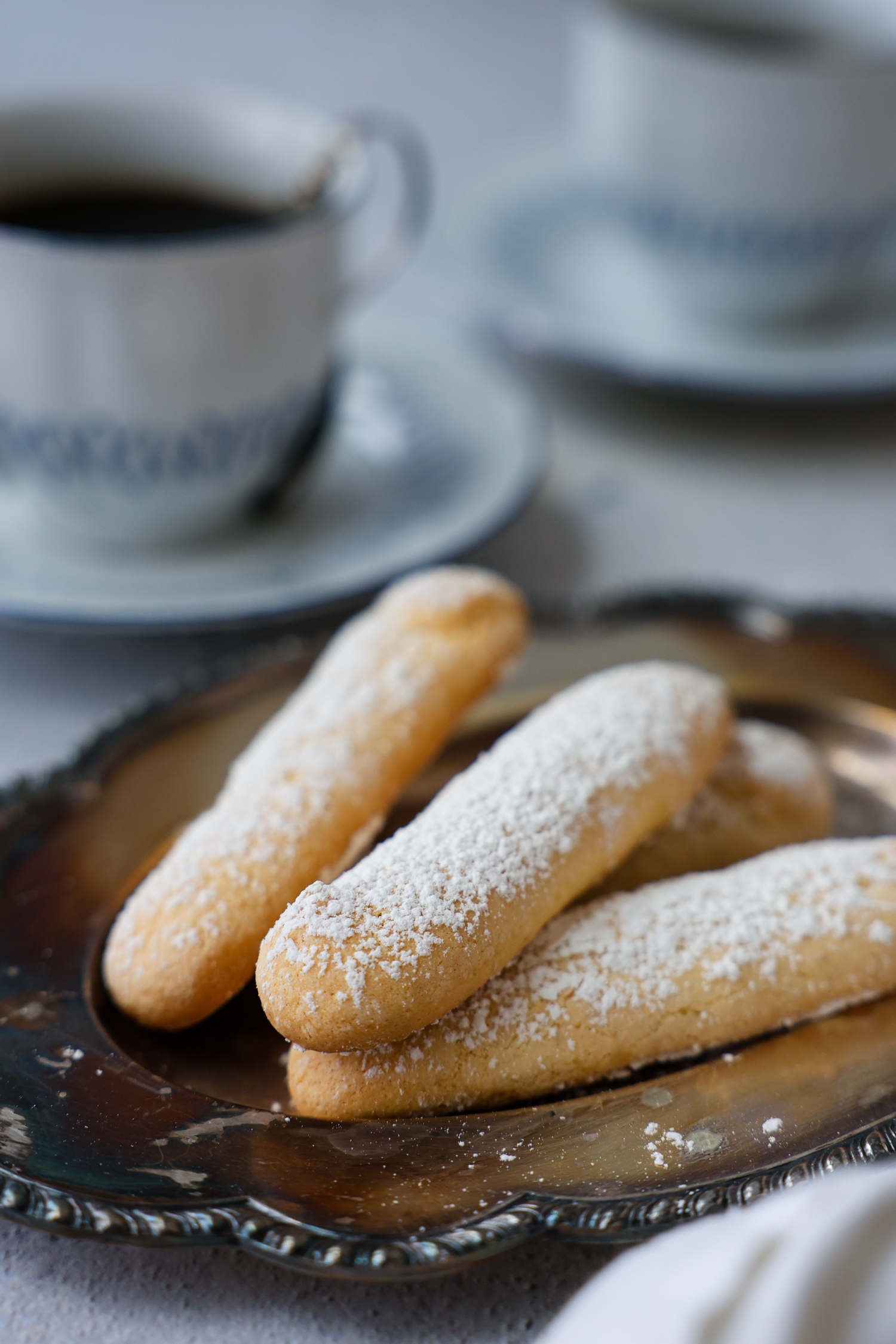 A pile of lady fingers dusted with sugar laying on a plate.