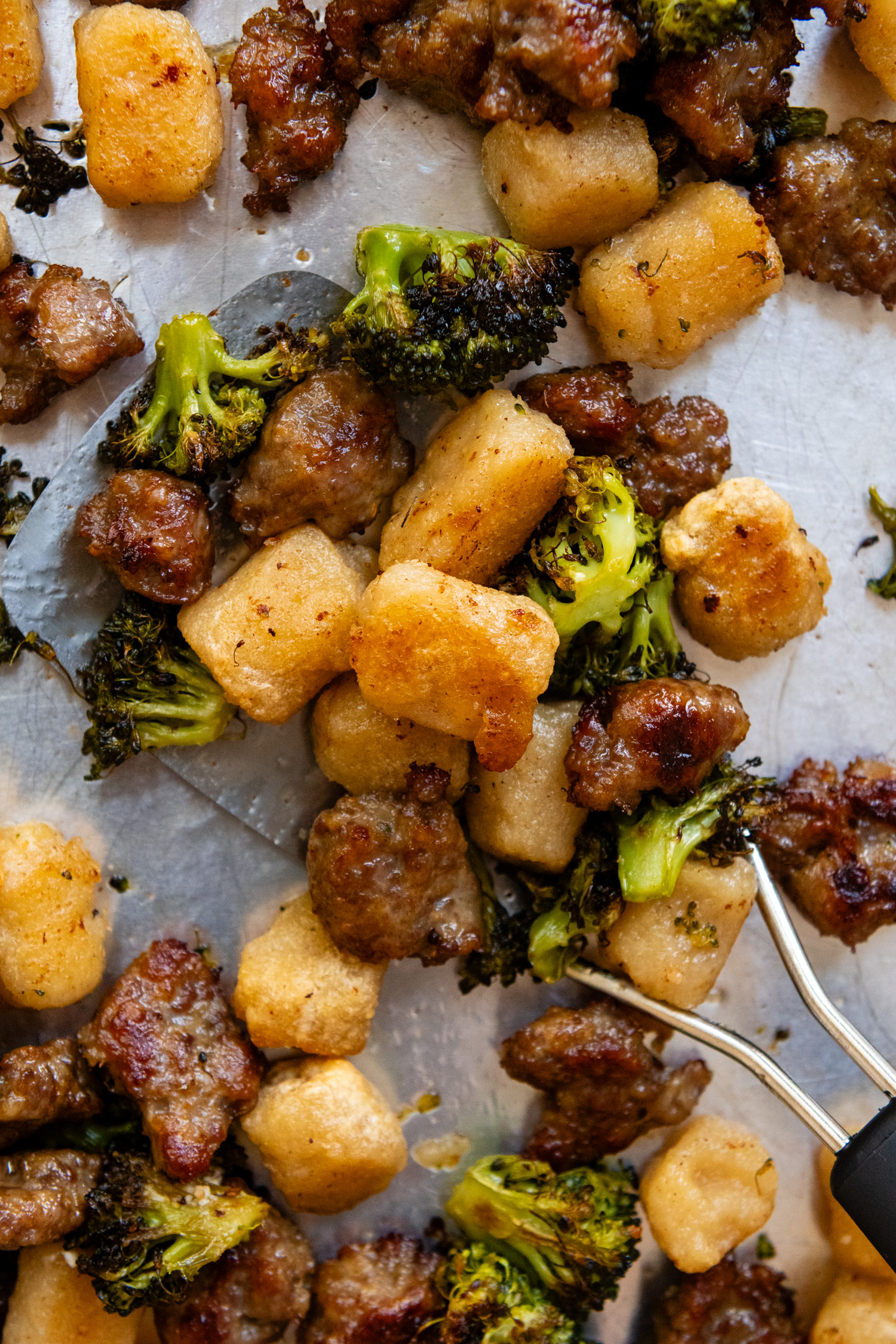 Close up of cooked gnocchi, broccoli and sausage on a metal spatula.