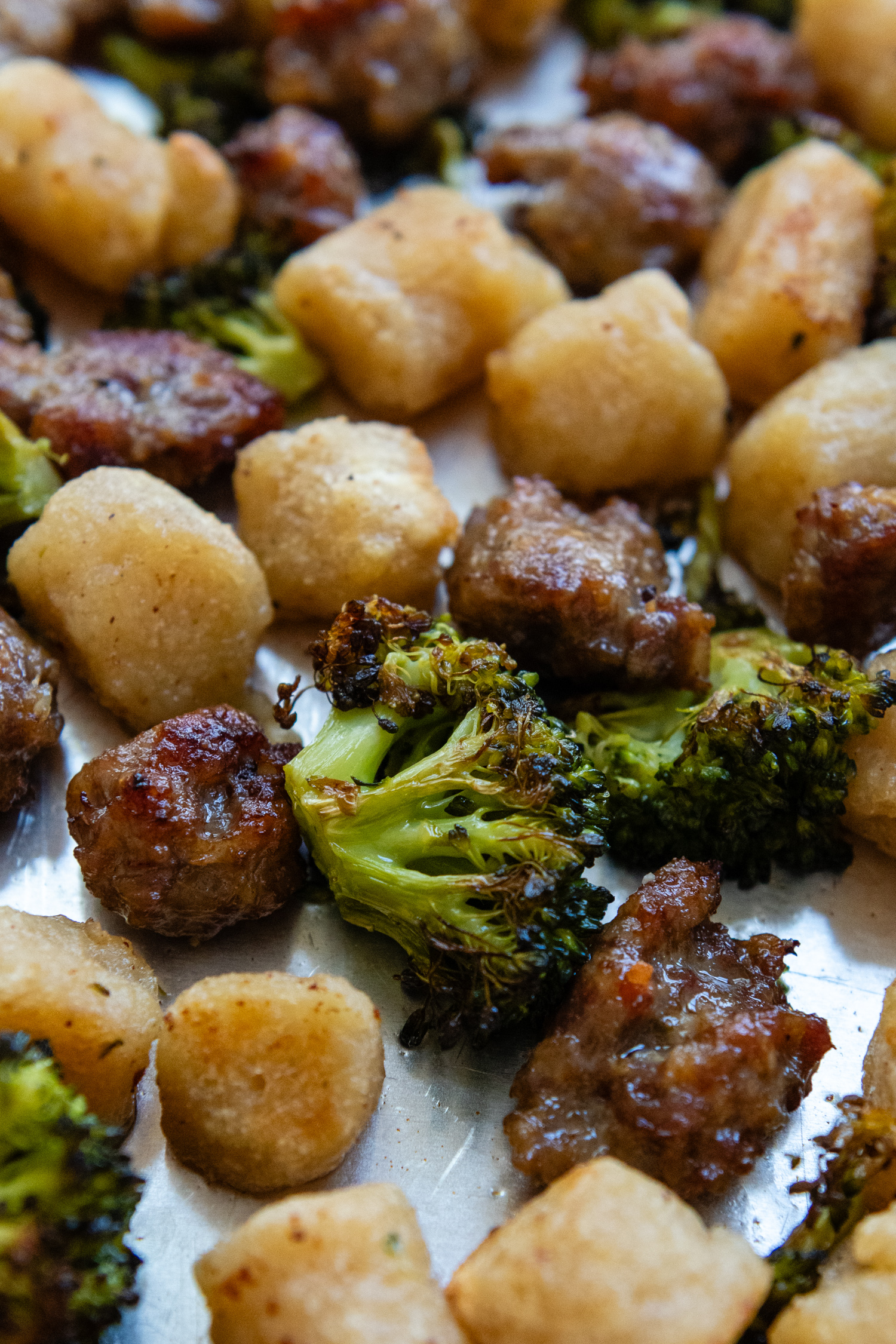 Close up of cooked gnocchi, broccoli and sausage on a sheet pan,