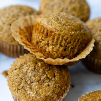 A stack of muffins with the wrapper coming off the top muffin showing texture.
