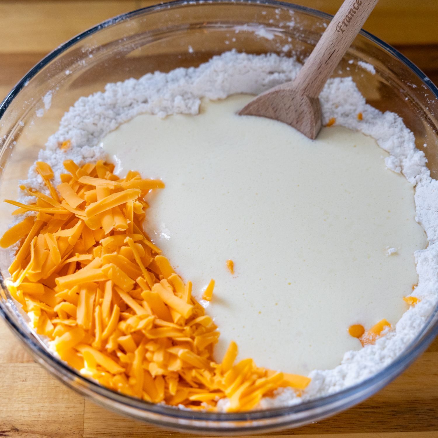 Bowl of dry biscuit ingredients, shredded cheese and milk.