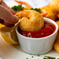 A hand dipping the crispy shrimp in a white dish of shrimp sauce.