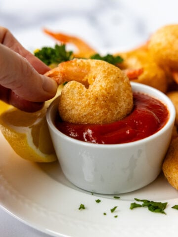 A hand dipping the crispy shrimp in a white dish of shrimp sauce.