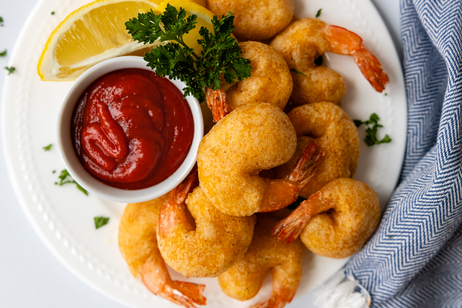 Overhead shot of crispy shrimp on a white plate with a dish of shrimp suace.