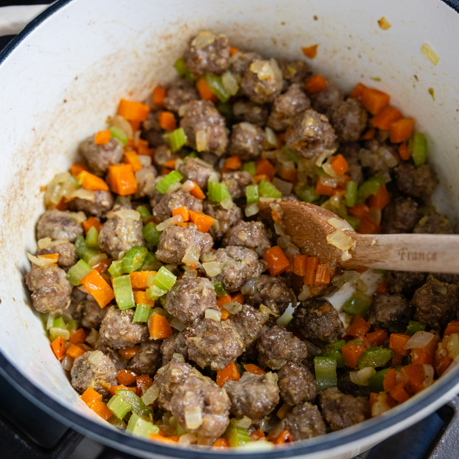 Meatballs and vegetables combined in stockpot.