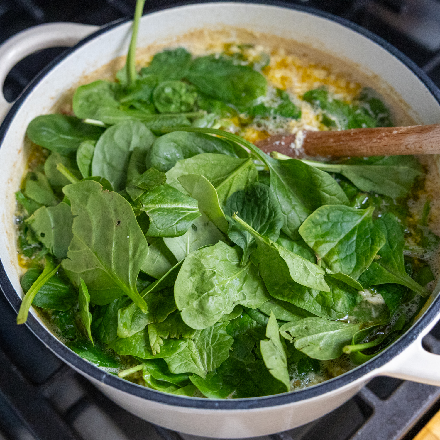 Spinach being folded into stockpot of ingredients.