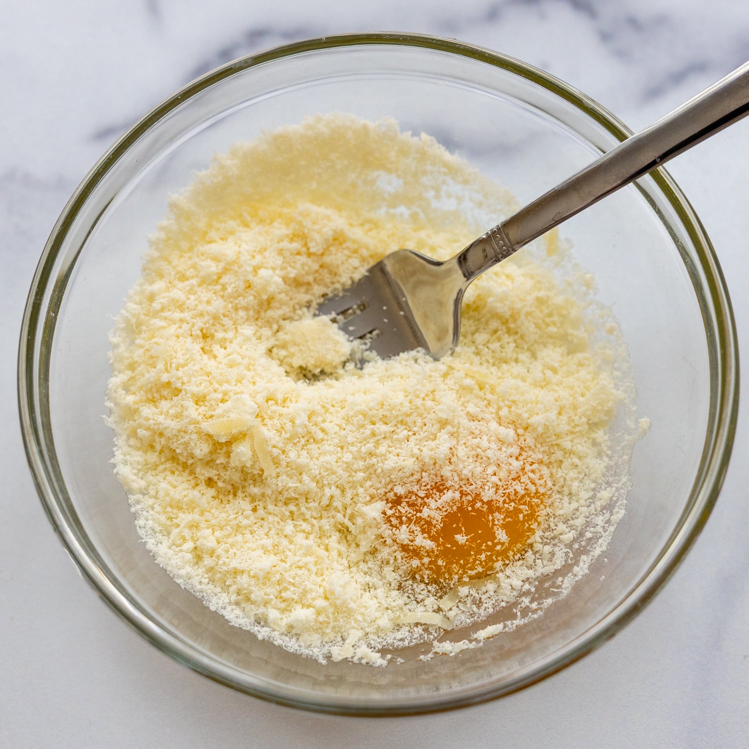 Egg and parmesan combined in glass bowl.
