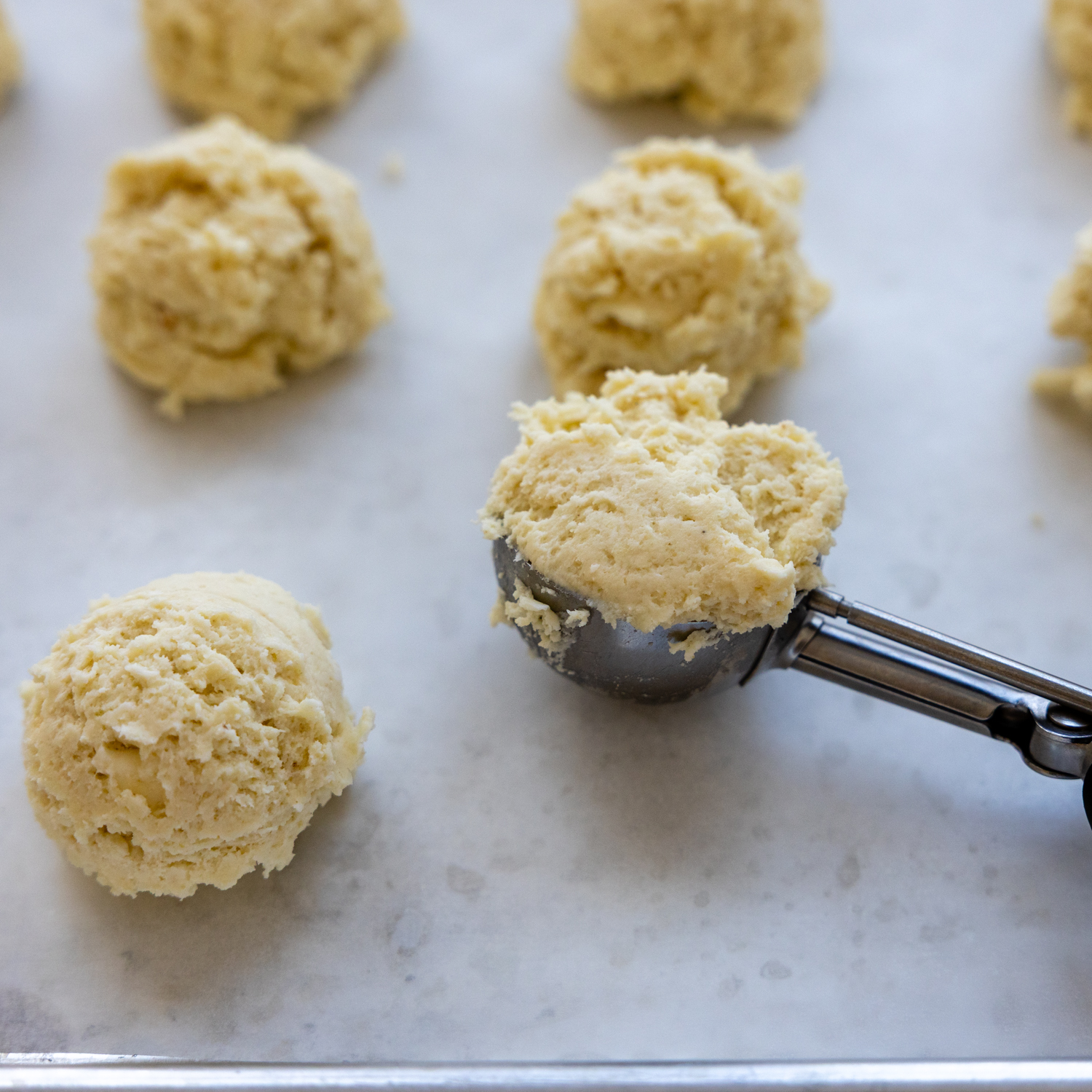 Biscuits dough being scooped and dropped onto parchment paper.