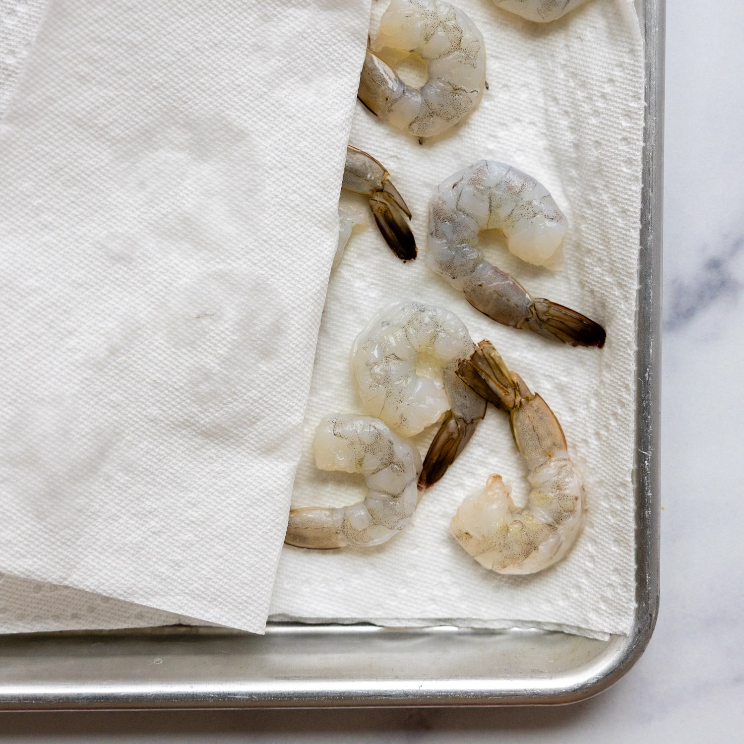 Shrimp being dried while laying between paper towels on pan.