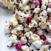 a Valentine's themed white chocolate popcorn mix with M&Ms on a white surface.