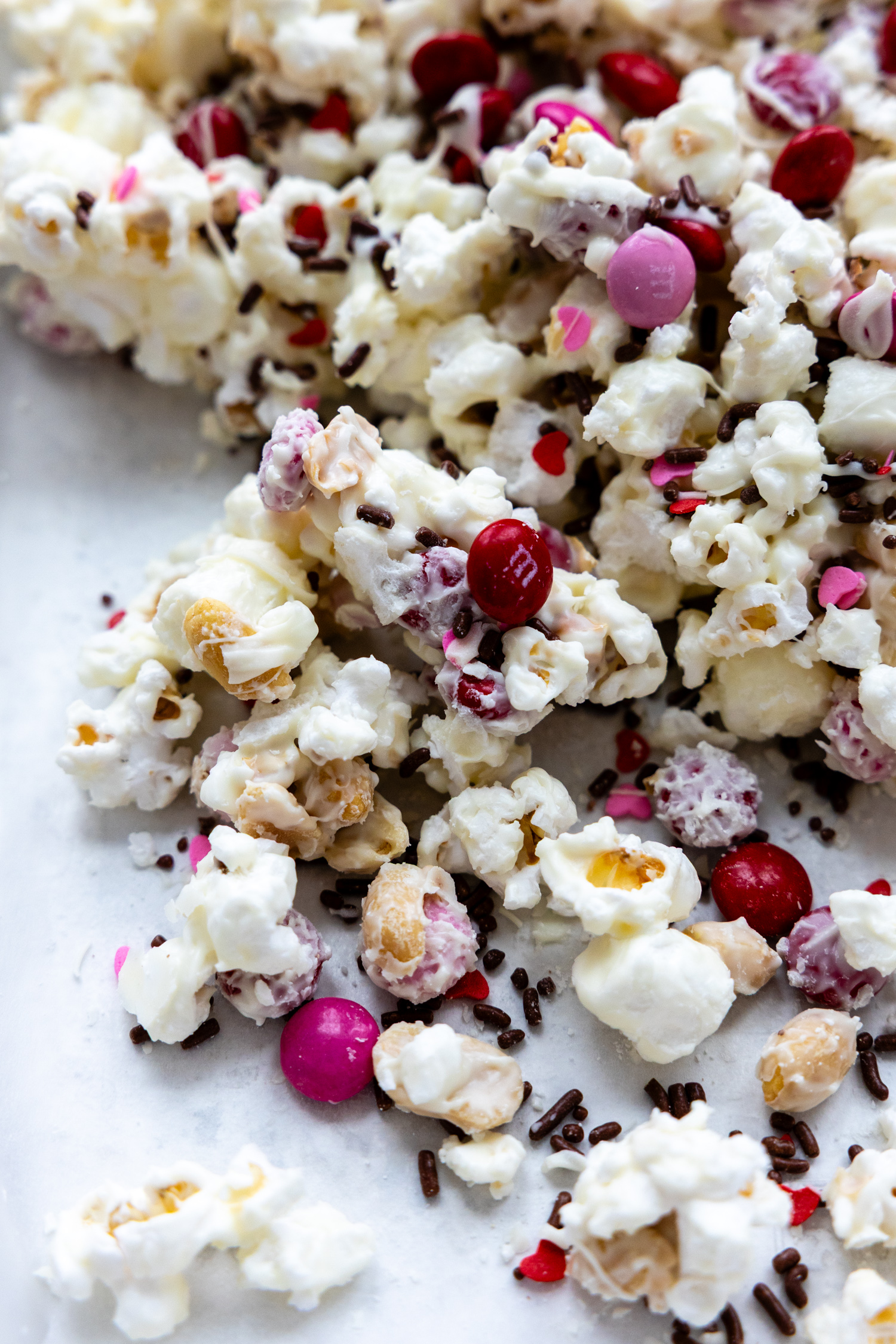 a Valentine's themed white chocolate popcorn mix with M&Ms on a white surface.