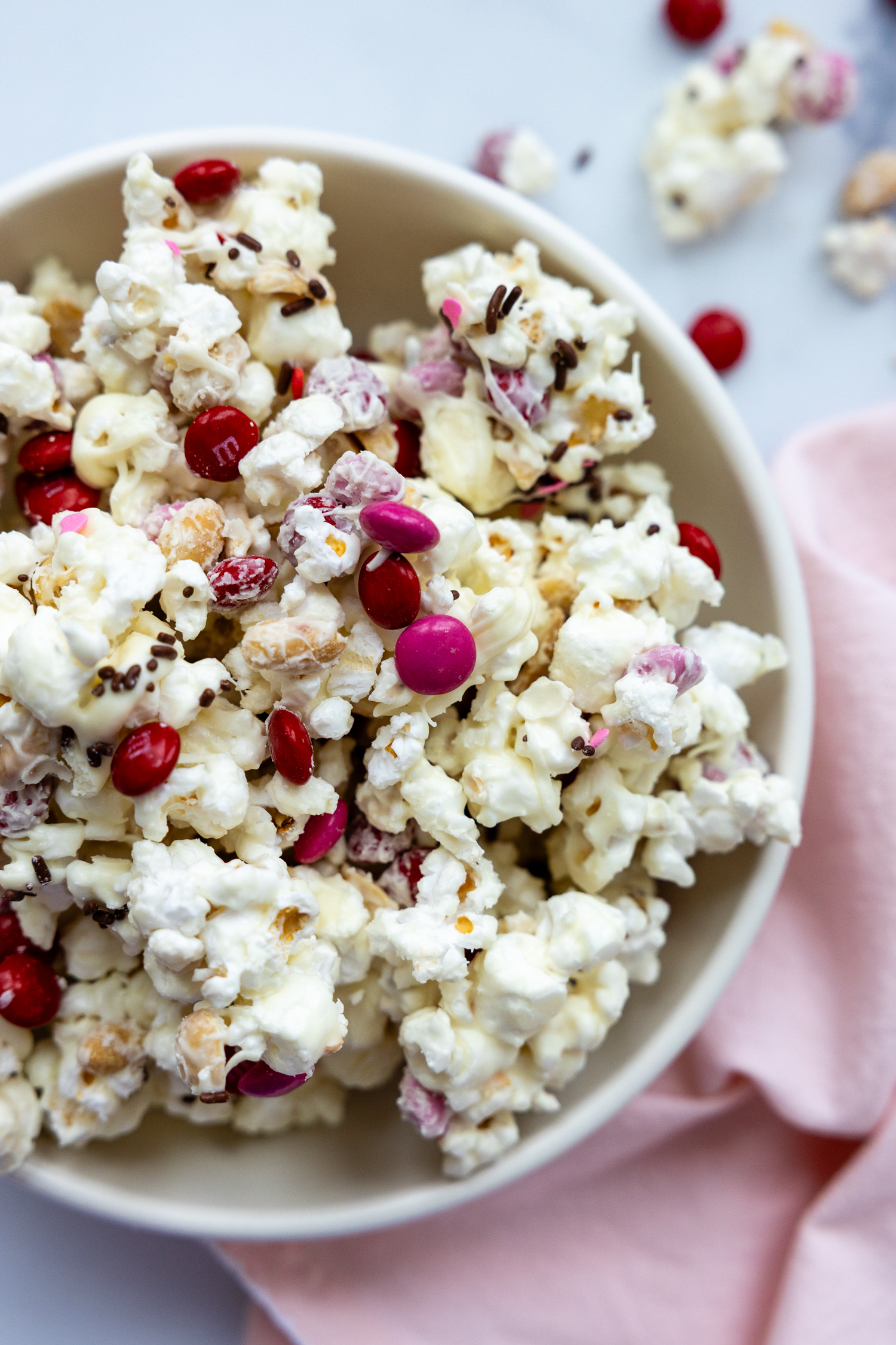 popcorn snack mix in a white bowl with a pink towel next to it.