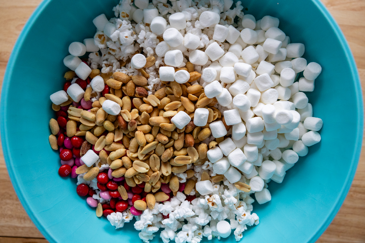 peanuts, marshmallows, M&Ms, and popcorn in a large teal bowl.