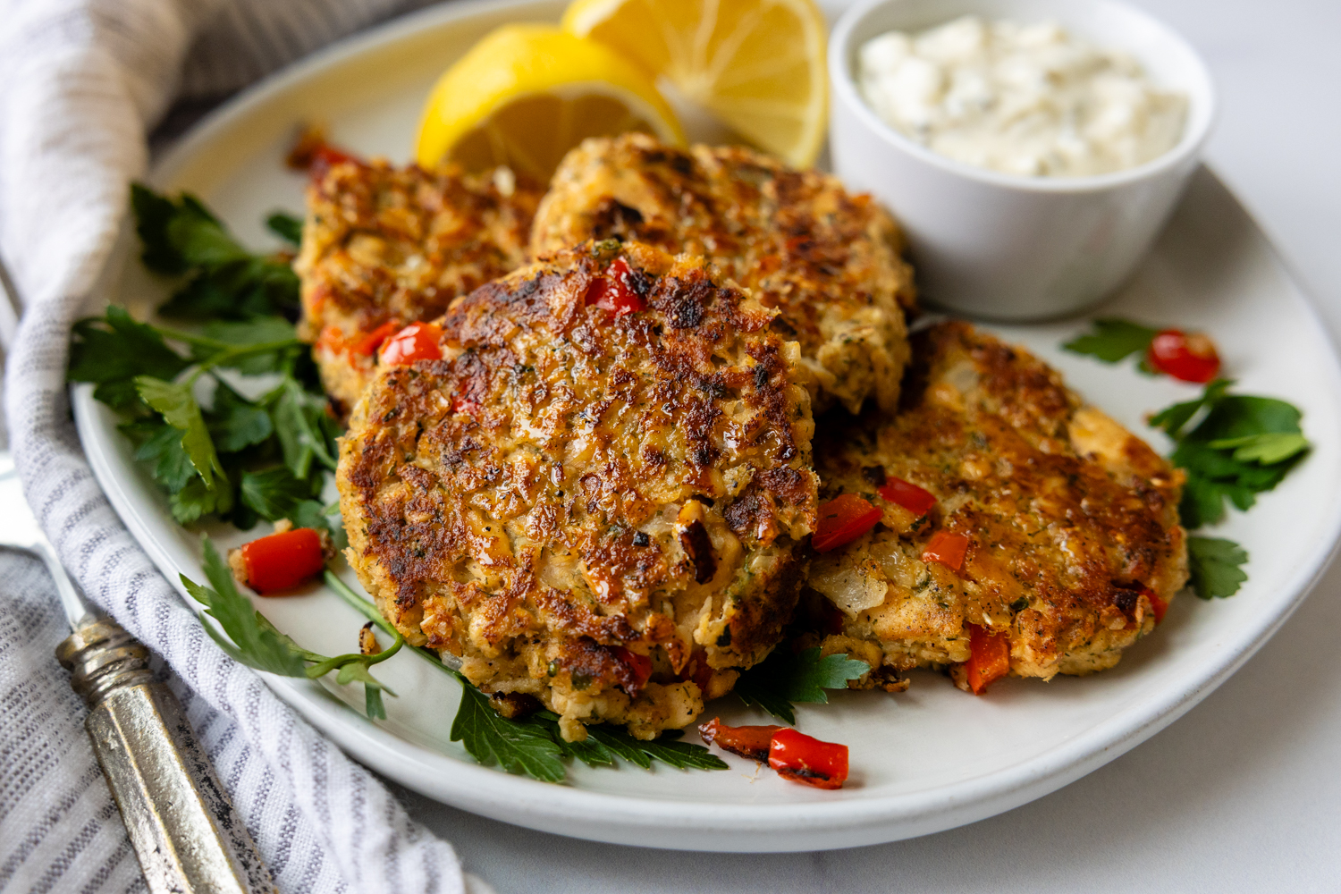 Overhead shot of salmon patties on a white plate with lemon garnish and a bowl of dipping sauce.