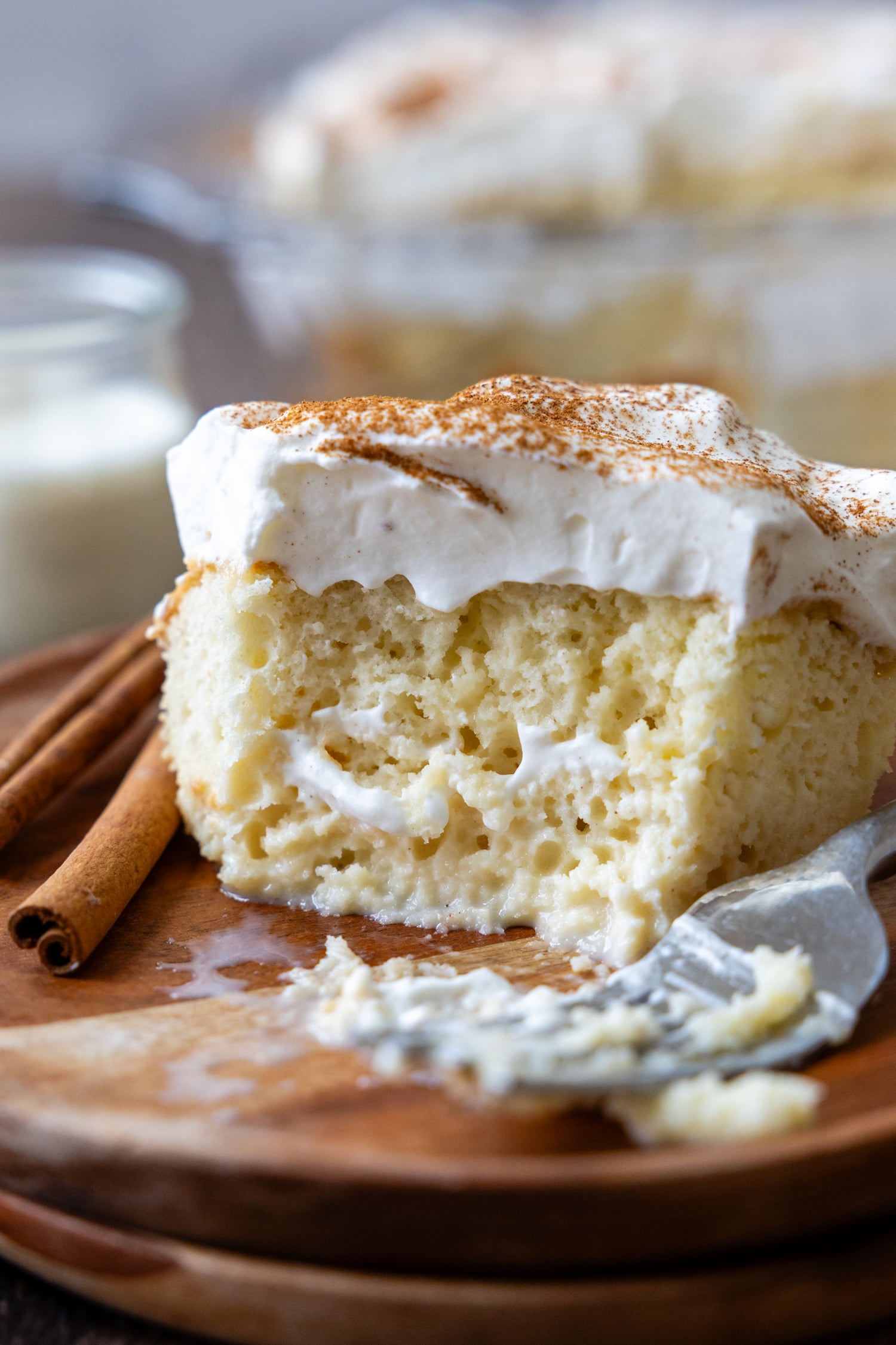 An slice of tres leches cake on a wooden plate with a bite removed showing the texture of the inside of the cake.