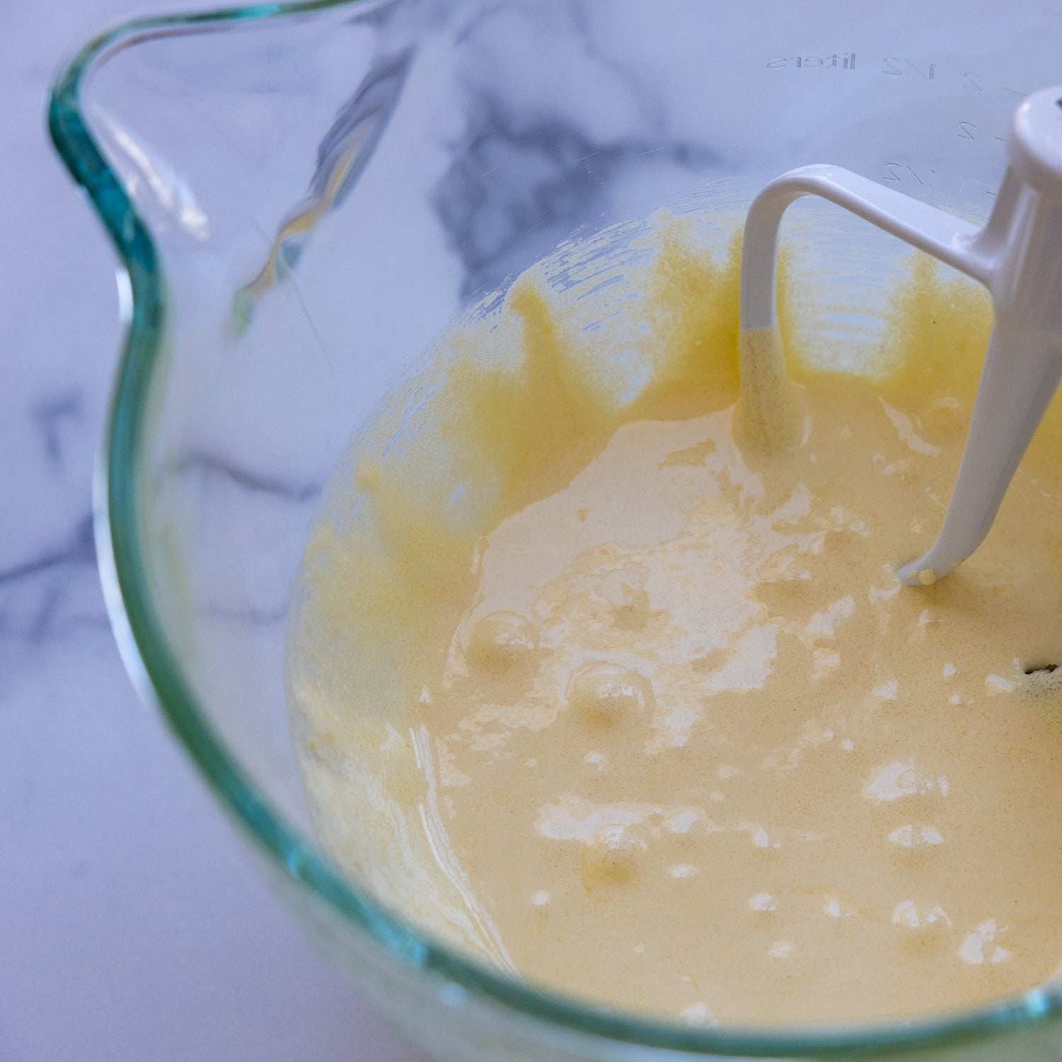 Egg yolk and sugar being mixed in a glass bowl.