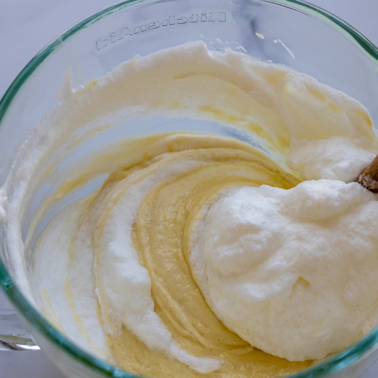 Egg yolk and sugar being mixed in a glass bowl.