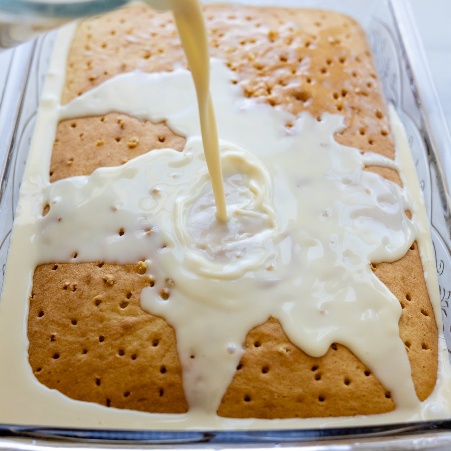 Cake with holes poked into it with the milk soak being pored on top.