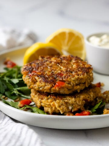 Gluten free salmon patties stacked on top of one another on a white plate.