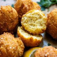 Cooked hush puppies with one cut in half showing inside texture.