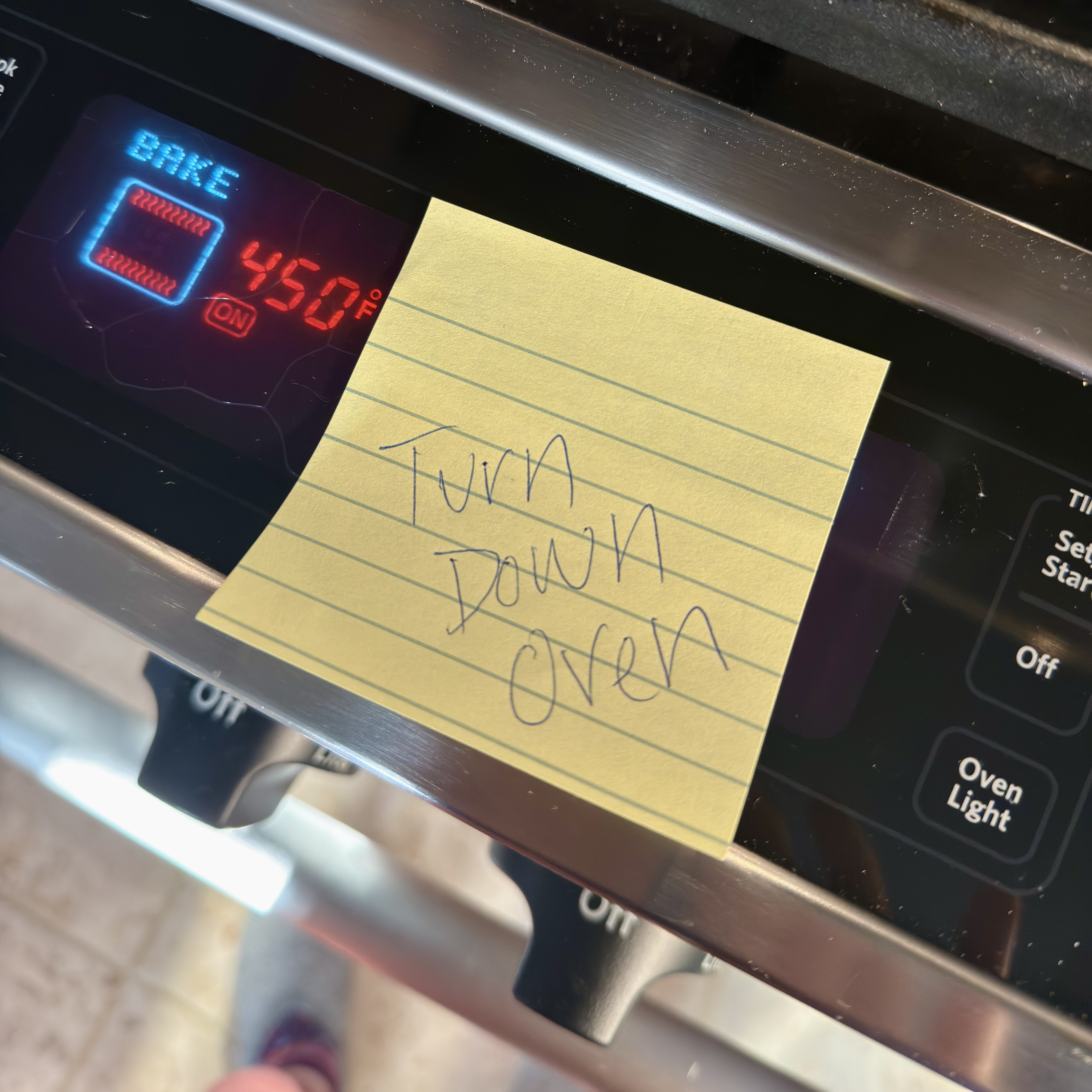 a sticky note on an oven reminding to turn down the temperature.