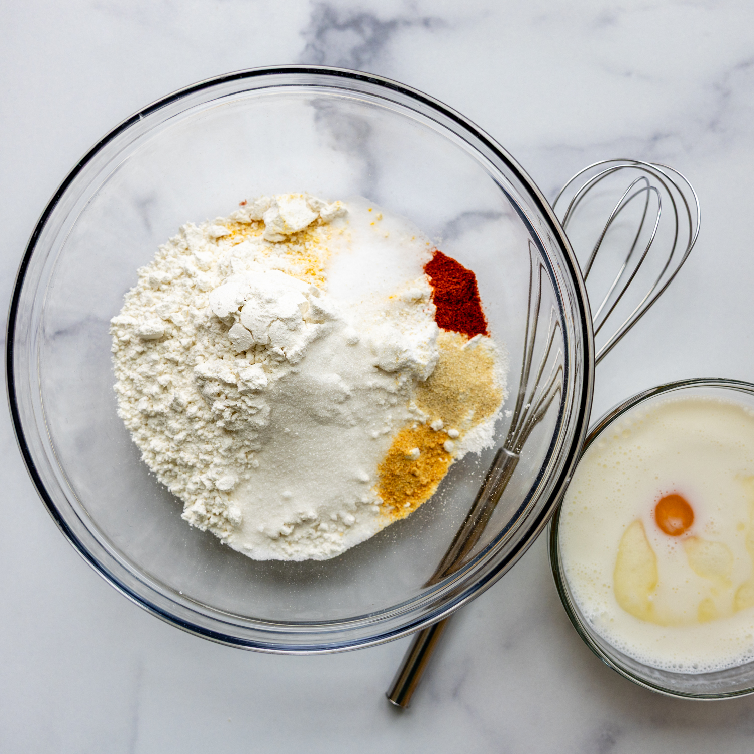 Glass bowl full of ingredients with a whisk.