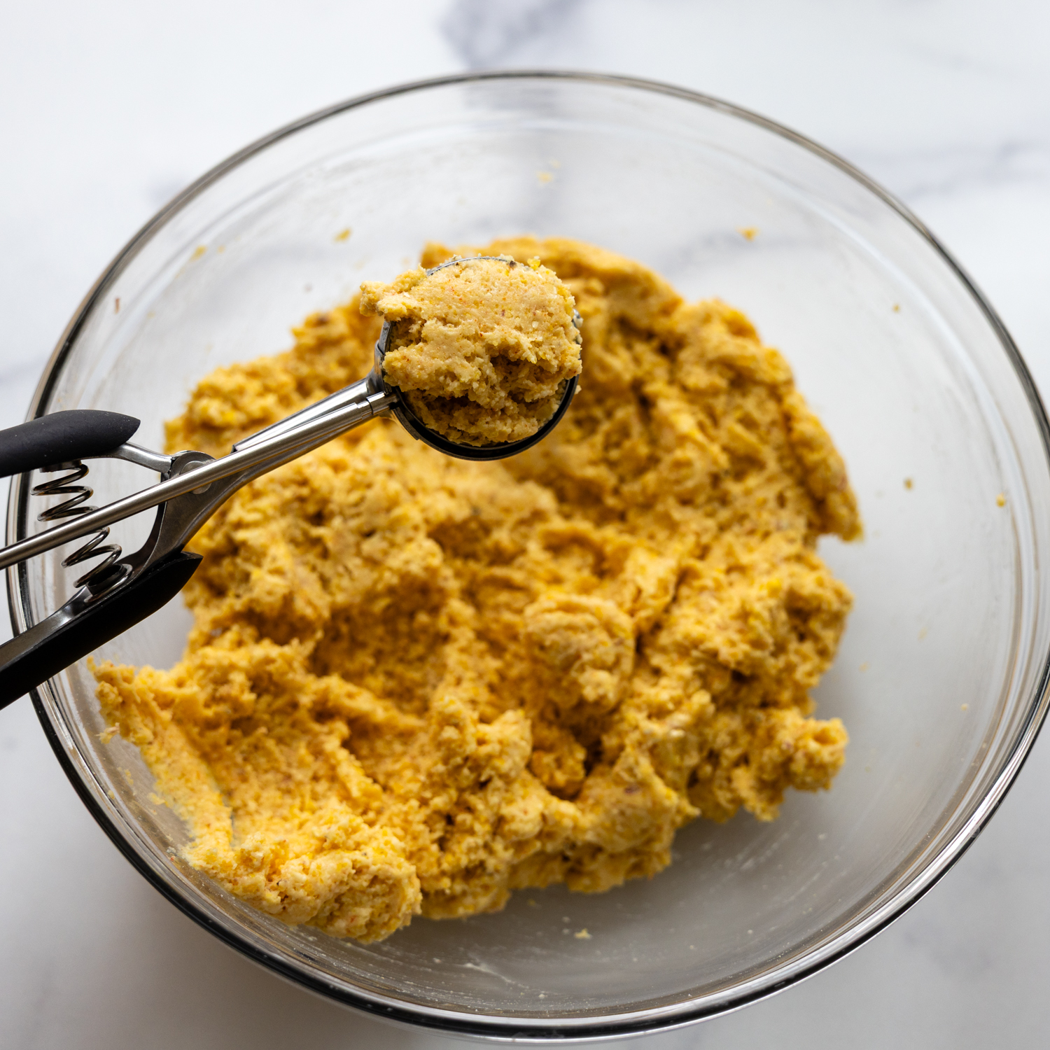 Combined ingredients in glass bowl being portioned by a scooper.