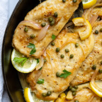 Gluten Free Chicken Piccata in a skillet with lemon garnish and topped with capers.