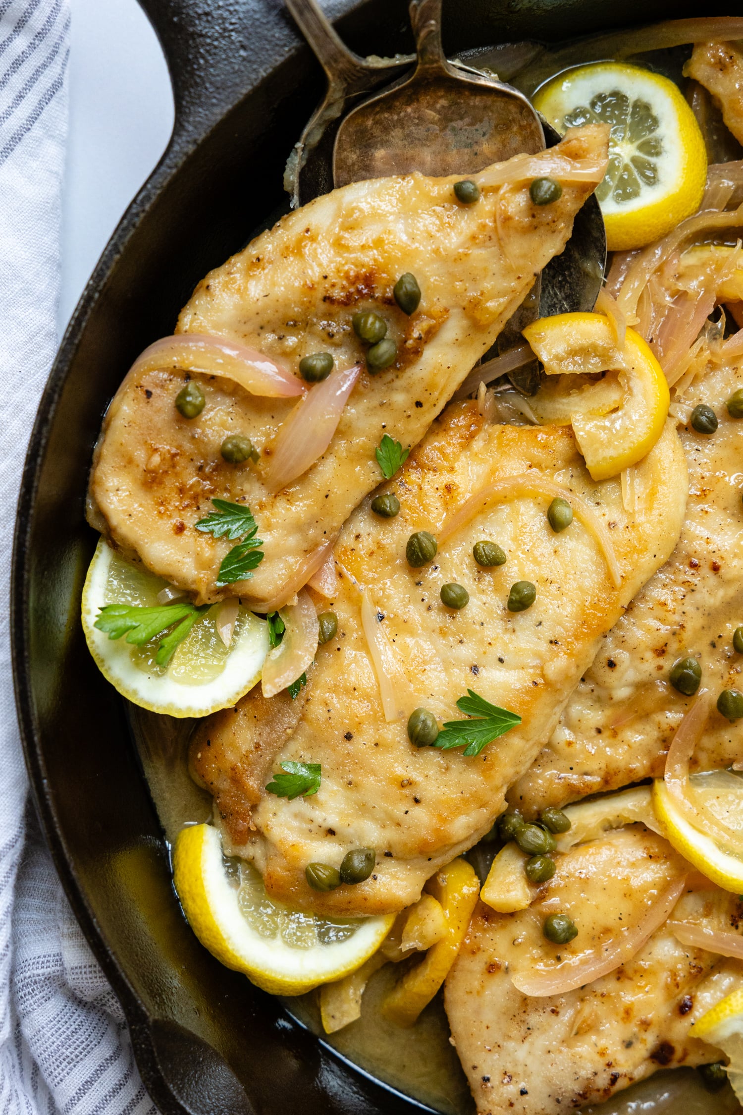 Gluten Free Chicken Piccata in a skillet with lemon garnish and topped with capers.