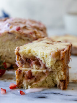 strawberry bread slice broken in half on a marble surface with glaze dripping down.